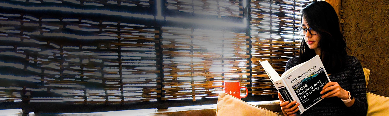 Female sitting criss-cross on a couch looking down at a Cisco Certification Guide Book