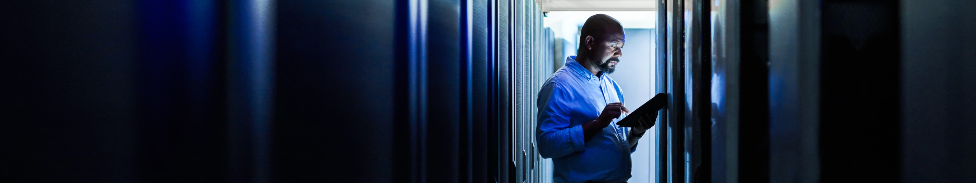 IT worker walking through the enterprise data center checking network dashboards on a tablet.