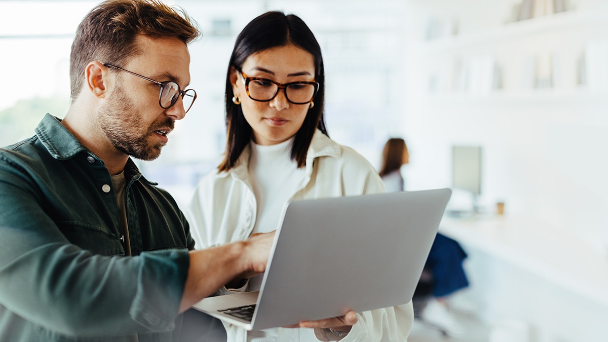 Two office workers wirelessly viewing laptop device 